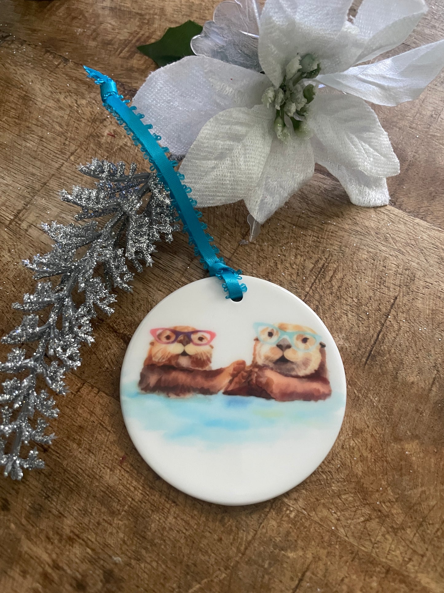a watercolor of Otters in Glasses holding hands on an orrnament