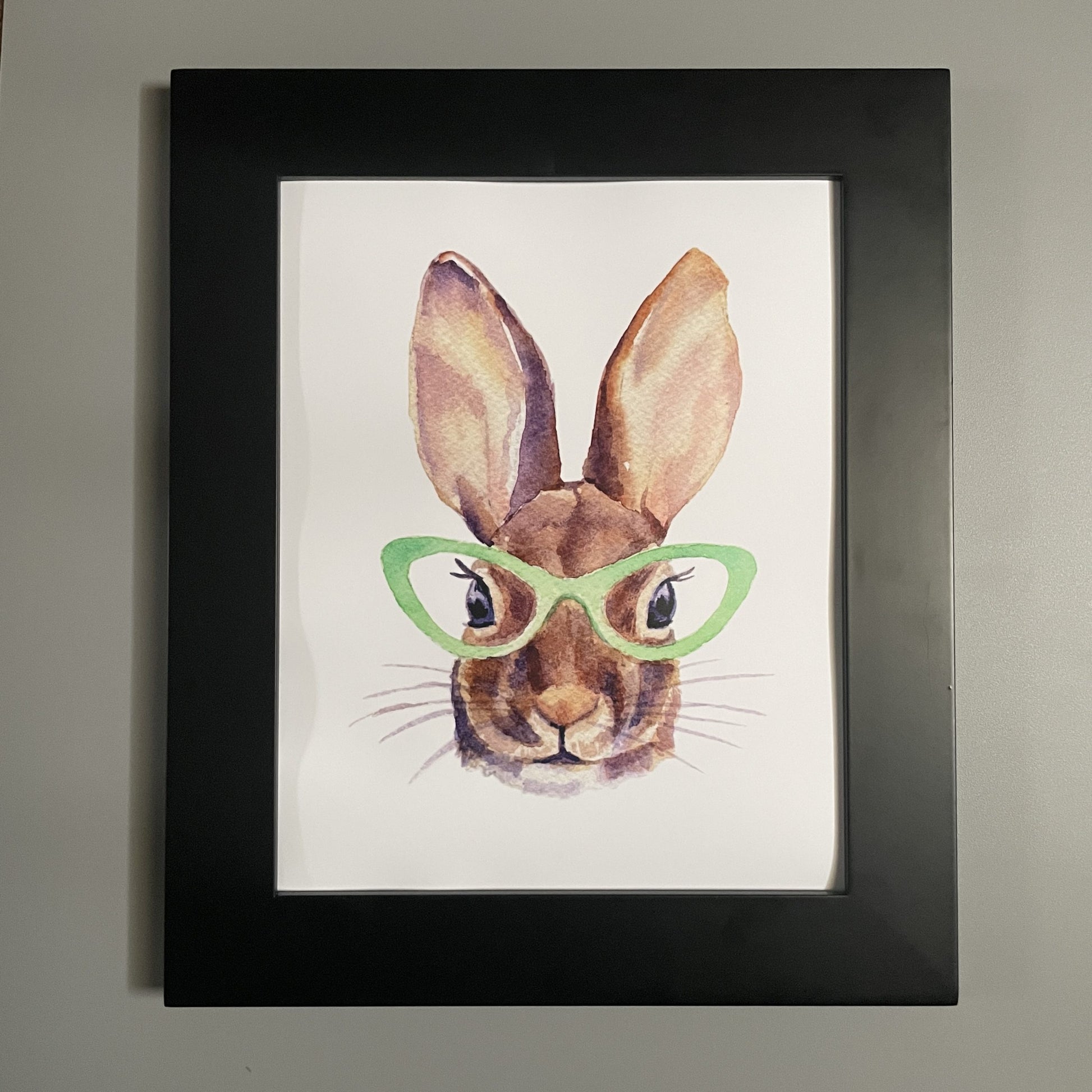 Print of a bunny wearing green glasses shown in a black frame.