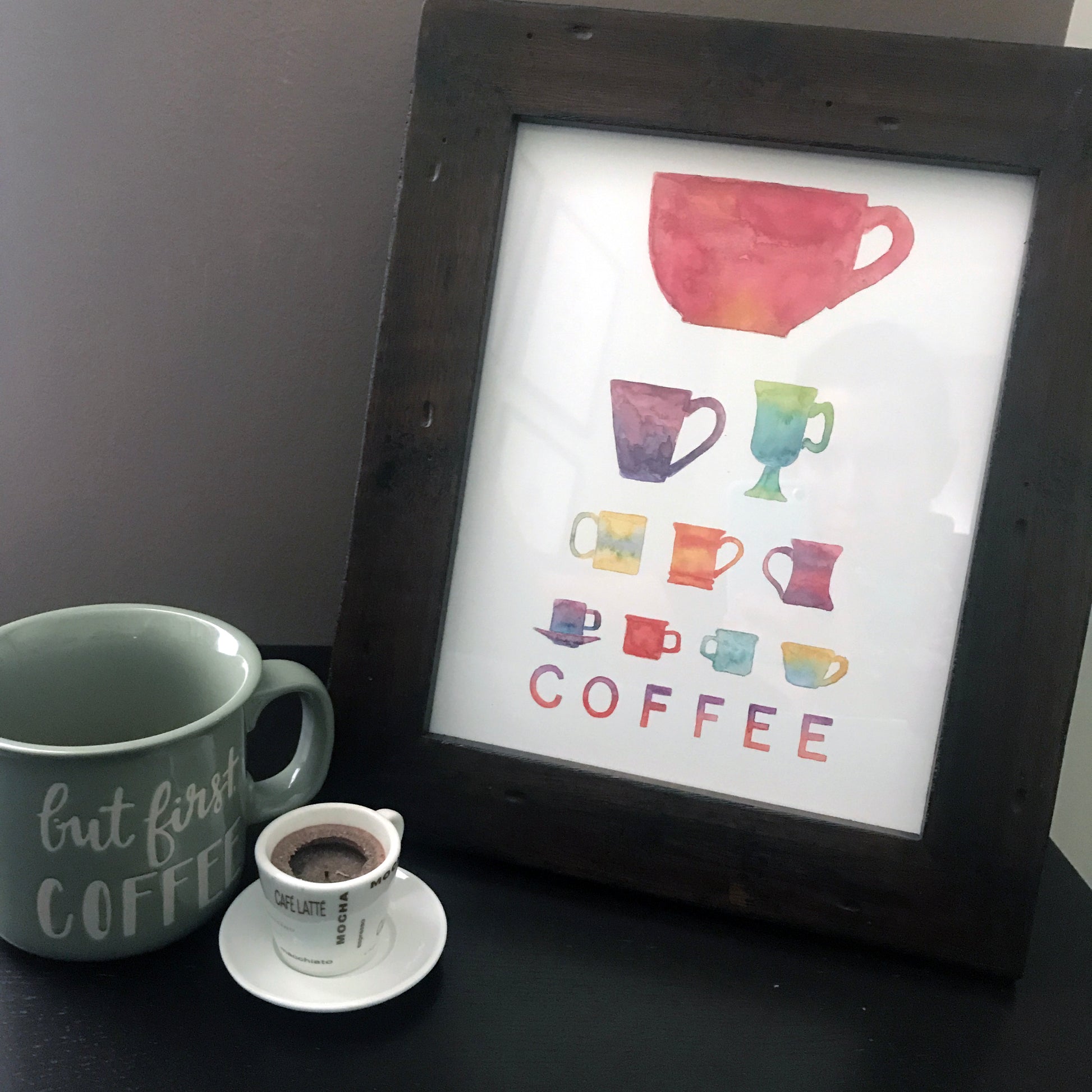 A print of colorful coffee cups in varying shapes and size in an eye chart. Print shown in a wood frame.