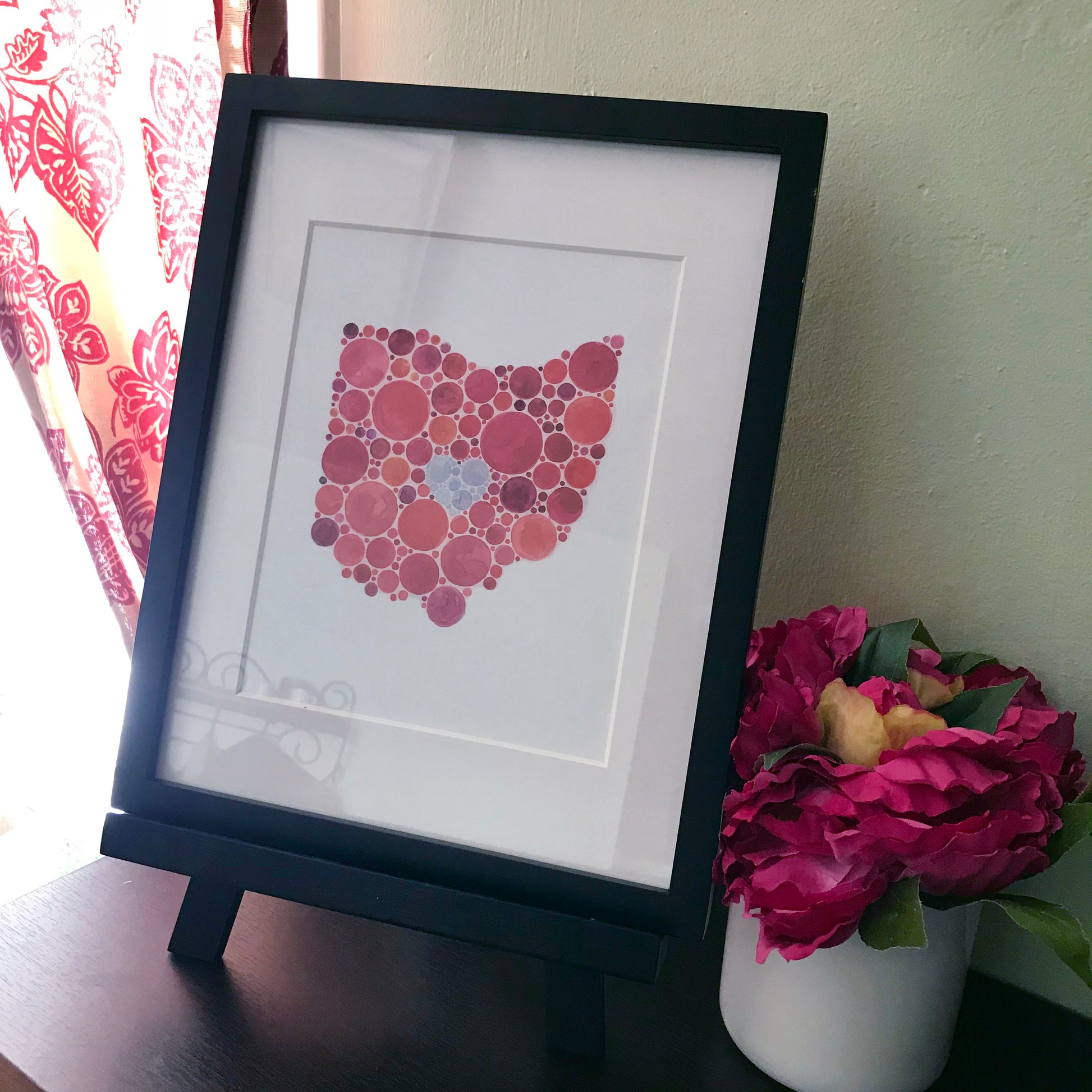 A print showing the state of Ohio done in the style of an ishihara color vision test in a black frame.